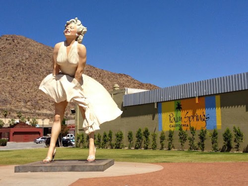 A large statue of Marilyn Monroe in a white dress, set against a blue sky and a colorful Palm Springs sign.