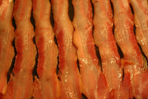 Close-up of cooked bacon strips arranged in a row, showcasing their crispy texture and glistening fat.