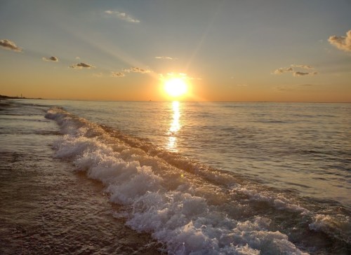 Sunset over calm waters, with gentle waves lapping at the shore and a warm golden glow in the sky.
