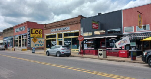 A street view of shops, including Dillon's, Lee's, and Haley Bros, with parked cars and a cloudy sky.