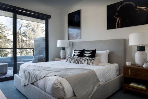 Modern bedroom with a large bed, decorative pillows, lamps, and artwork, featuring a balcony view.