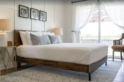 A cozy bedroom featuring a wooden bed, decorative pillows, and large windows with sheer curtains.
