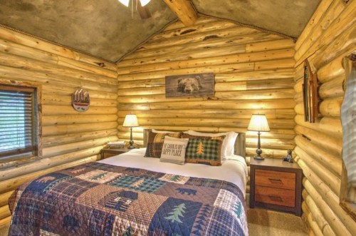 Cozy log cabin bedroom with a quilted bedspread, wooden walls, and two lamps on nightstands.