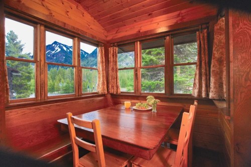 Cozy wooden dining area with a table set for breakfast, featuring mountains and trees visible through large windows.