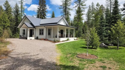 A charming house with a metal roof surrounded by trees and a gravel driveway, set in a lush green landscape.