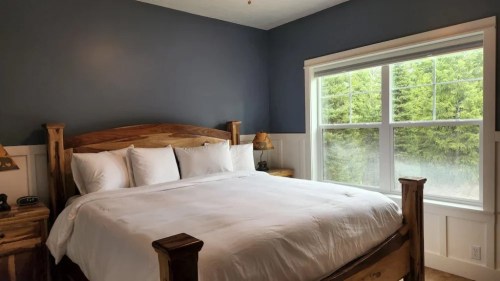 Cozy bedroom with a wooden bed, white bedding, and a large window overlooking greenery.