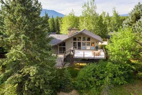 A modern house surrounded by trees, featuring a large deck and mountain views in the background.