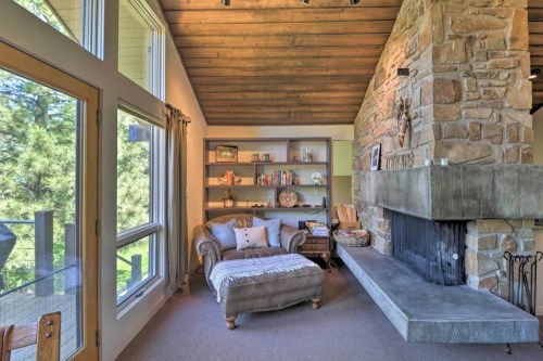 Cozy living room with stone fireplace, wooden ceiling, and bookshelves, featuring a comfortable couch and natural light.