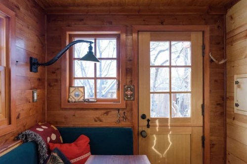 Cozy wooden interior with a door, windows, and a small seating area featuring cushions and wall decor.