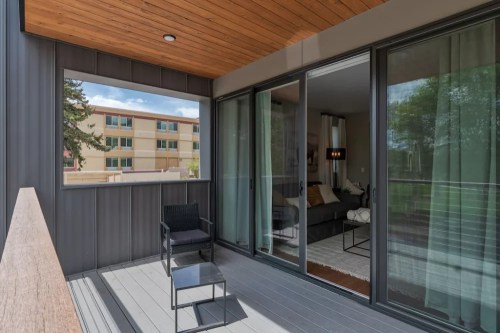 A modern balcony with a wooden ceiling, featuring a chair and a view of a living room through glass doors.