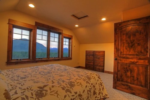 Cozy bedroom with a floral bedspread, wooden furniture, and large windows showcasing a mountain view.