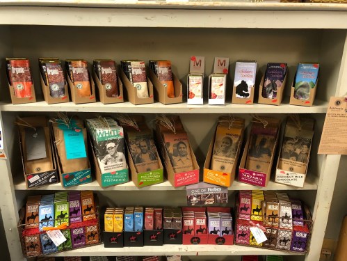 A shelf displaying various chocolate bars in colorful packaging, organized by type and origin.