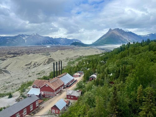 A scenic view of a red-roofed building complex surrounded by mountains and lush greenery under a cloudy sky.