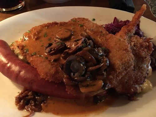 A plate featuring breaded fried meat topped with mushroom sauce, served with a sausage and red cabbage.