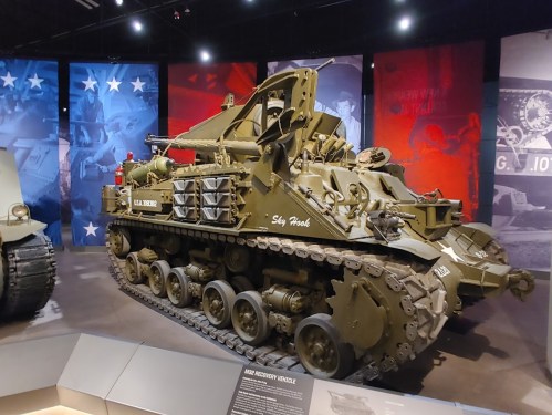 A military tank displayed in a museum, featuring a green exterior and various equipment mounted on it.