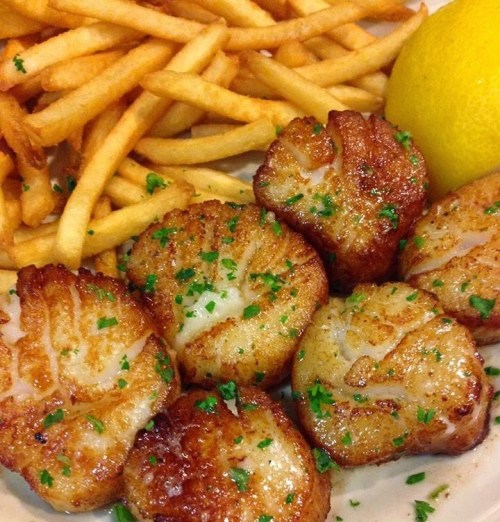 A plate of golden-brown scallops garnished with parsley, served with crispy fries and a lemon wedge.
