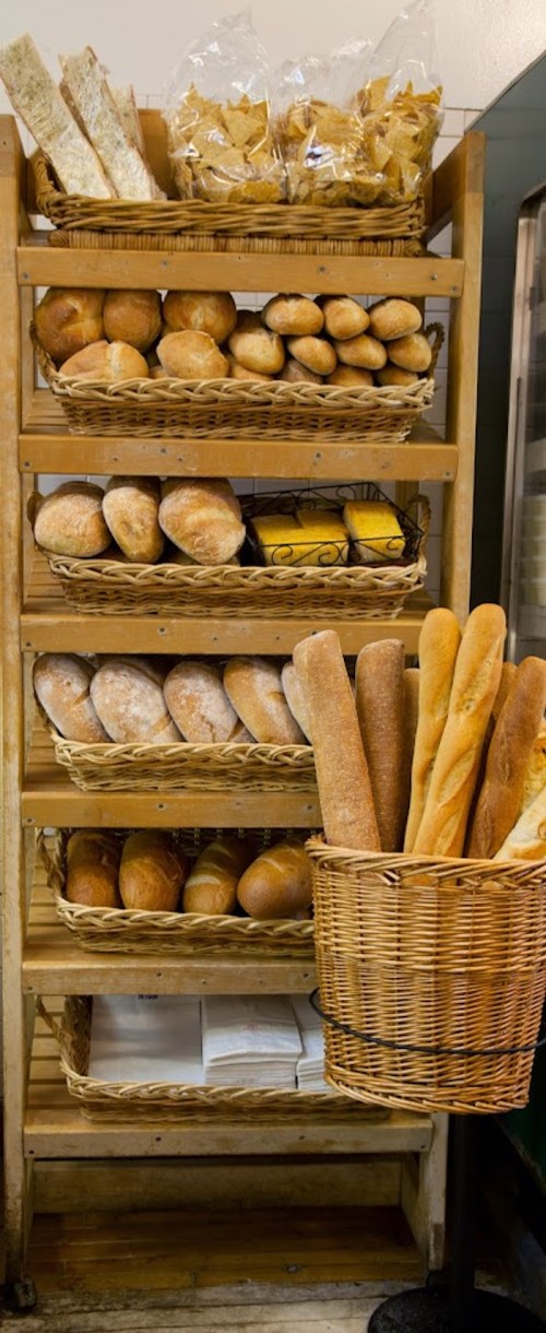 A wooden shelf filled with various types of bread and baked goods, including rolls and baguettes in a basket.