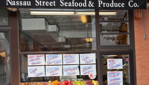 A storefront with a sign reading "Nassau Street Seafood & Produce Co." and various handwritten signs about available products.