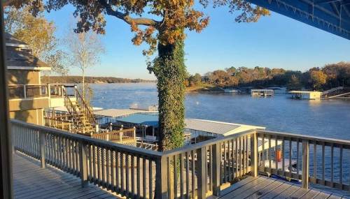 Scenic view of a lake with docks, trees, and a clear blue sky from a wooden deck.