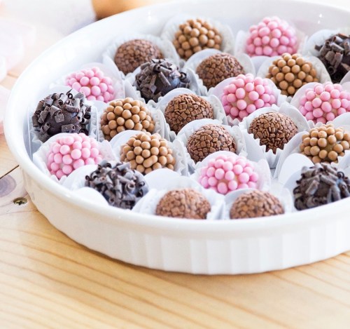 A white platter filled with assorted chocolate truffles topped with colorful sprinkles in pink and brown hues.