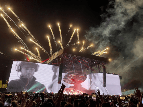 A concert scene with a large stage, fireworks, and an audience holding up phones, capturing the performance.