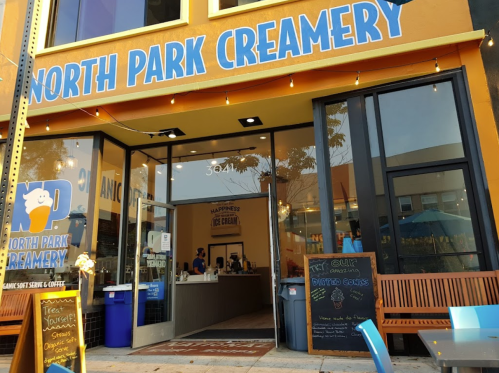 Exterior of North Park Creamery, featuring a bright sign, open door, and outdoor seating area.