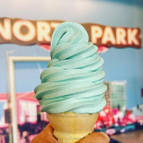 A hand holding a soft-serve ice cream cone with light blue swirled ice cream against a colorful background.
