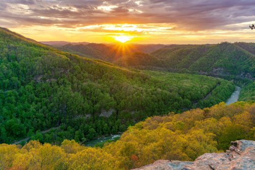 A stunning sunset over lush green mountains and a winding river, with vibrant clouds in the sky.