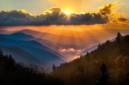 A breathtaking sunset over misty mountains, with rays of sunlight breaking through clouds and illuminating the landscape.