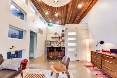 Modern interior featuring a cozy living area, kitchen, and wooden ceiling with large windows and stylish decor.