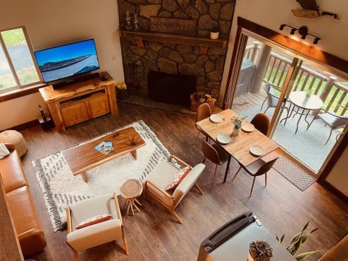 Cozy living room with a stone fireplace, wooden furniture, and a view of a deck through sliding glass doors.