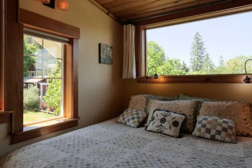 Cozy bedroom with a quilted bed, large window, and views of greenery outside. Natural light fills the space.