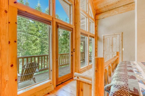 Cozy interior with large windows, wooden accents, and a view of a forested balcony.