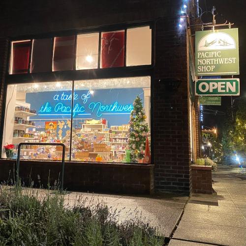 A brightly lit shop window displays festive decorations and products, with a sign reading "Pacific Northwest Shop - OPEN."
