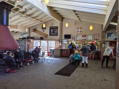 Interior of a cozy lodge with a fireplace, seating areas, and people ordering food at a counter.