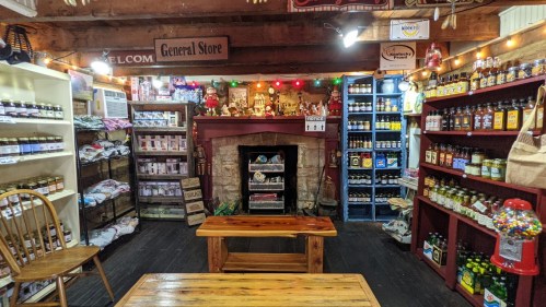 A cozy general store interior with shelves of jars, bottles, and a fireplace, decorated with lights and rustic charm.
