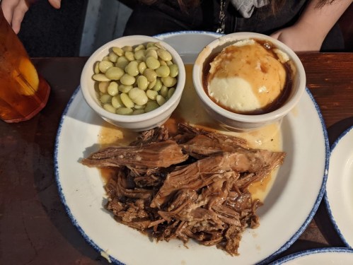 A plate with tender shredded beef in sauce, served with mashed potatoes and green beans in bowls on the side.