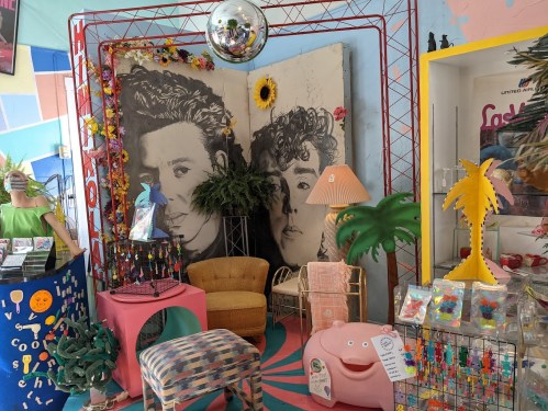 Colorful retro decor featuring large portraits, plants, and quirky furniture in a vibrant space.