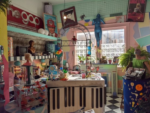 A colorful, eclectic room filled with vintage decor, a piano-shaped counter, and various quirky items and plants.