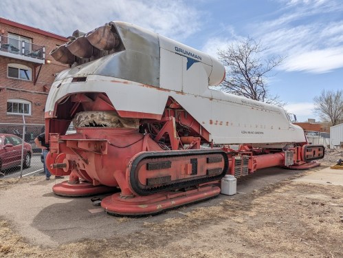 A large, vintage snowmobile with a distinctive design, parked outdoors near a building and surrounded by a fence.
