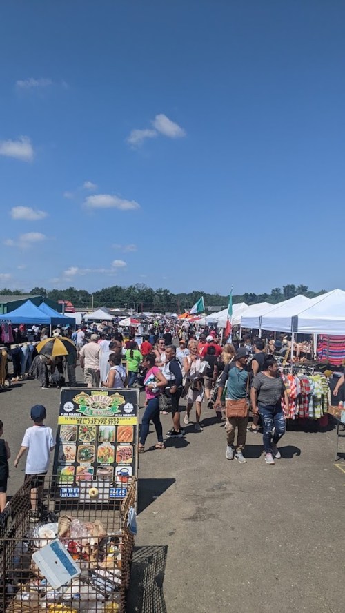 A bustling outdoor market with colorful tents, vendors, and a crowd of people enjoying the sunny day.