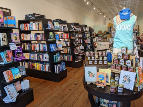 A cozy bookstore interior with shelves of books, a display table with candles, and a blue cap that says "BOOKS."
