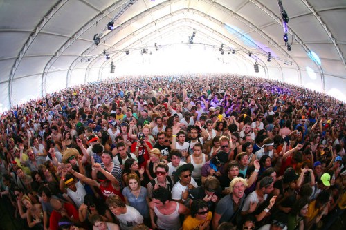 A large crowd of people enjoying a music festival inside a spacious tent, with vibrant energy and excitement.