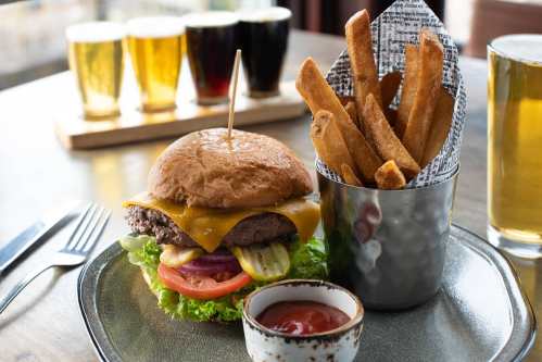 A juicy cheeseburger with lettuce, tomato, and pickles, served with crispy fries and a small bowl of ketchup.