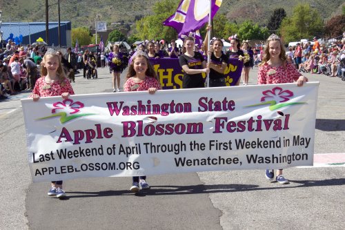 A parade scene with participants holding a banner for the Washington State Apple Blossom Festival in Wenatchee, WA.