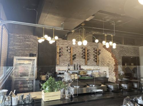 Modern restaurant interior featuring a stylish bar, pendant lights, and a display of wine bottles on the wall.