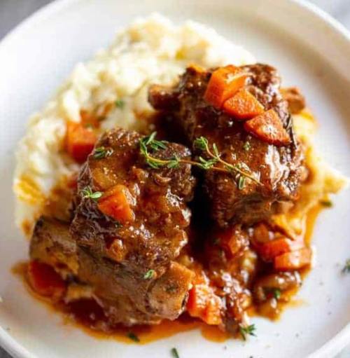 Tender braised meat with carrots served over creamy mashed potatoes, garnished with fresh thyme.
