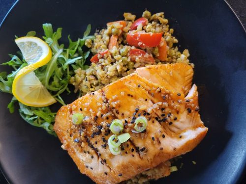 A plate featuring grilled salmon with green onions, served with a side of vegetable rice and arugula, garnished with lemon.