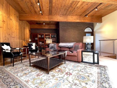 Cozy living room with wooden walls, a brick accent, plush sofa, glass coffee table, and stylish lighting.