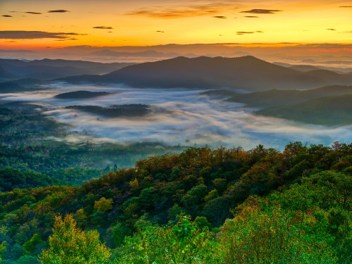 A breathtaking sunrise over misty mountains, with lush green hills and valleys bathed in warm golden light.
